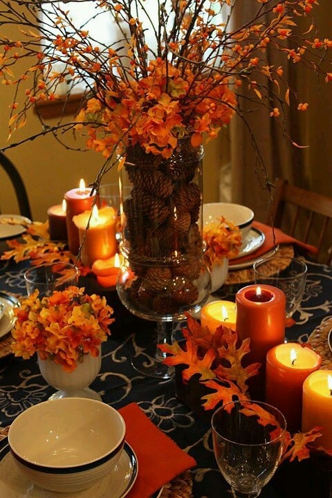 A rust colored fall table setting with fall leaves and blooms, a floral centerpiece and rust candles