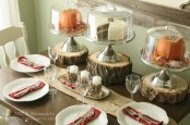 a very simple fall tablescape with a centerpiece of candles and nuts, tree stumps with cloches and pumpkins in them