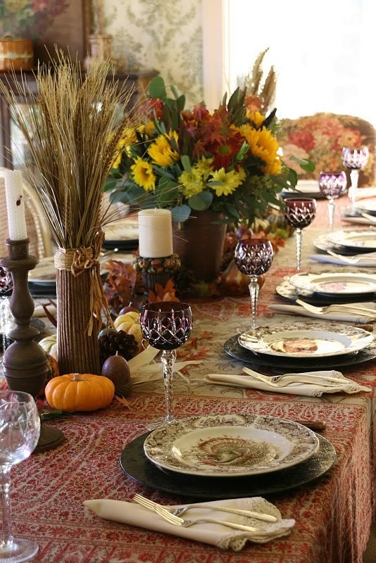 A vintage inspired tablescape with a printed tablecloth, faux pumpkins, pinecones, wheat and floral arrangements and printed plates