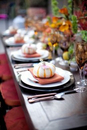 a fall tablescape with dark chargers, glasses, bright napkins and faux pumpkins for each place setting