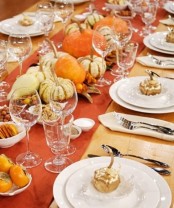 a colorful fall tablescape with an orange table runner, real pumpkins and veggies for decor and not only