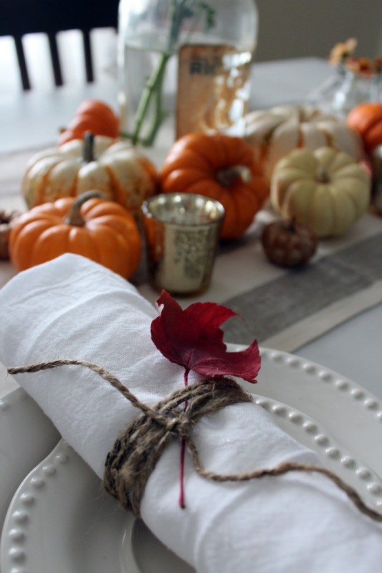 faux pumpkins for a centerpiece and a napkin wrapped with twine and fall leaves make the tablescape bold and fall-like
