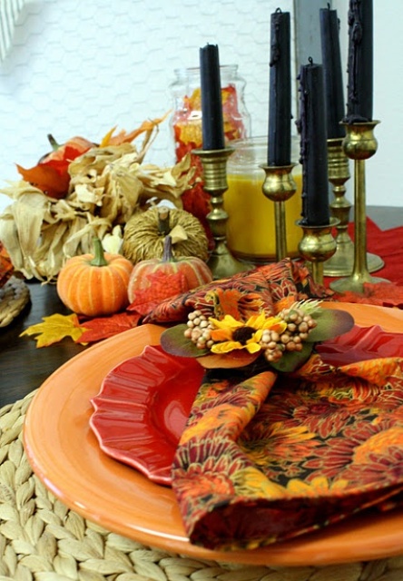 a bright tablescape with printed plates, woven placemats, fabric pumpkin and corn husks centerpiece and tall black candles