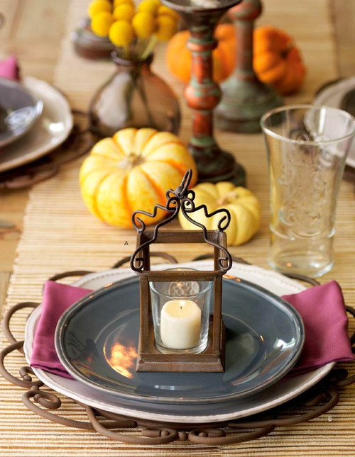 a colorful fall table setting with a purple napkin, a candle mini lantern, faux pumpkins and a woven table runner