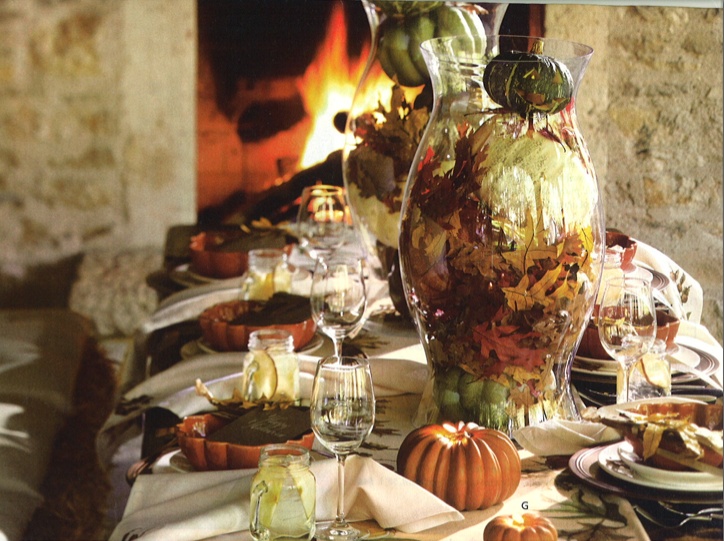 A vintage inspired tablescape with pumpkin plates, faux pumpkins, fall leaves and large glass jars with fall leaves