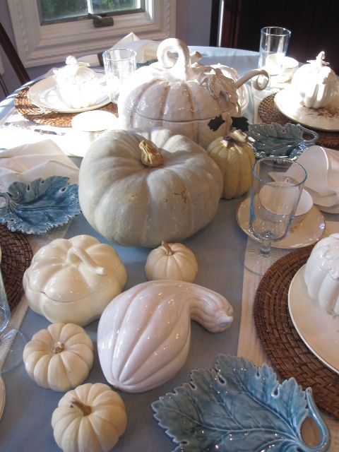 a blue and white tablescape with natural and faux pumpkins, a blue table runner and leaf plates plus woven placemats