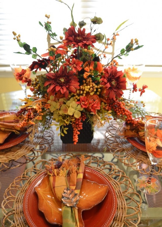 a rust, orange and green tablescape with a lush floral centerpiece with berries and woven placemats and colorful plates