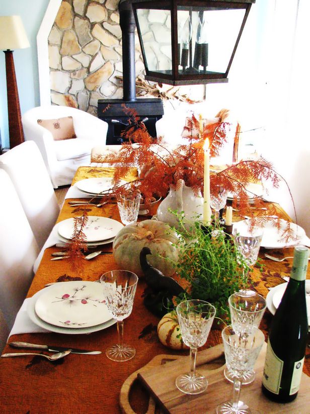 A bold fall tablescape with a rust colored tablecloth, natural pumpkins and greenery, tall candles