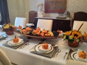 a simple fall tablescape with silver chargers and napkins, a wooden bowl with faux pumpkins and gourds and some blooms