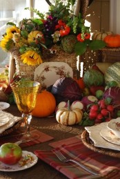 a harvest tablescape with plaid napkins, woven placemats and a lush floral and vegetable centerpiece with a bakset and a plate