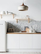 a Scandinavian kitchen done in creamy, with sleek white cabinets, a white fridge, white countertops and a white marble hex tile backsplash