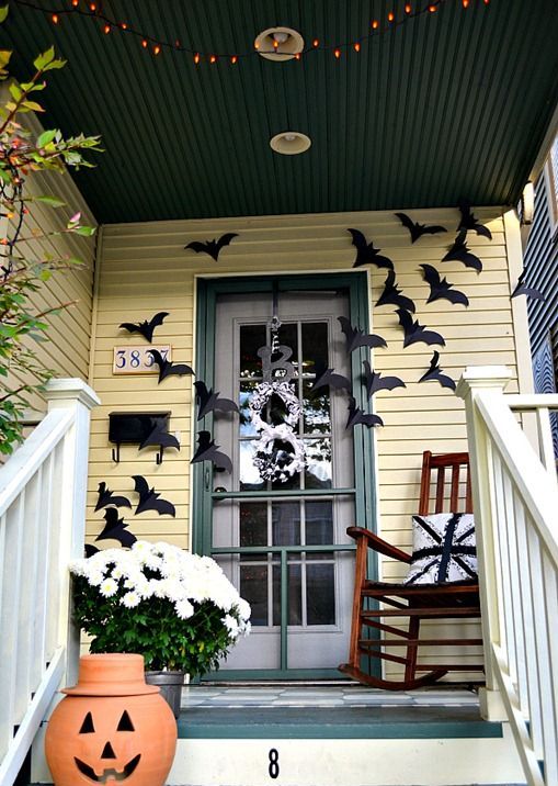 a Halloween front door covered with black paper bats and with a terracotta pumpkin and white blooms in a planter are cool