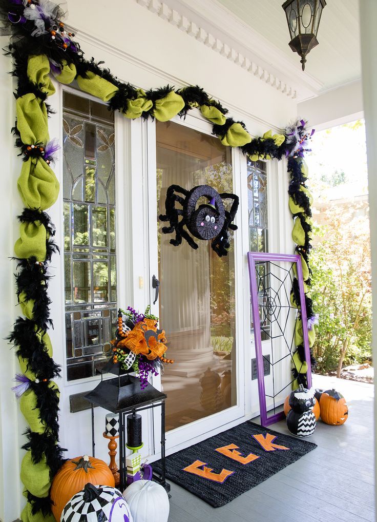 An extra bold Halloween front door decorated with neon green and black garlands, a black spider, black, white and orange pumpkins, a candle lantern topped with a bold bow
