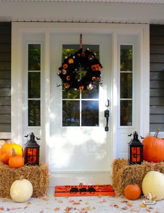 a rustic Halloween porch with hay, pumpkins, candle lanterns and a bright orange and black wreath looks awesome