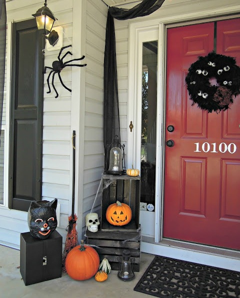 a Halloween front porch decorated with orange pumpkins, a black cat head, a witch's broom, spiders and a black wreath with googly eyes
