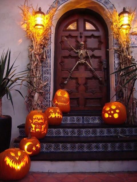 A Halloween porch decorated with jack o lanterns, corn husks and a skeleton right on the door is a unique idea