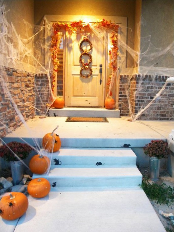 a rustic Halloween porch with bright fall leaves, pumpkins and vine wreaths plus realistic spiderweb is an easy and cool idea