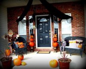 a Halloween front porch with black wicker furniture, pumpkins and planters, eyes on the door and black fabric over the door