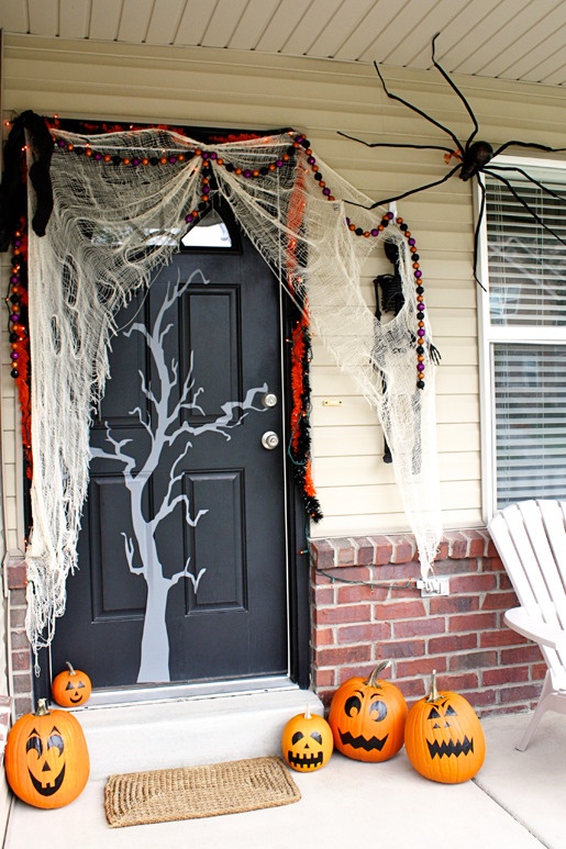 a Halloween front door with spiderweb, a tree silhouette, a light and bead garland, black spiders and some painted pumpkins is a cool idea