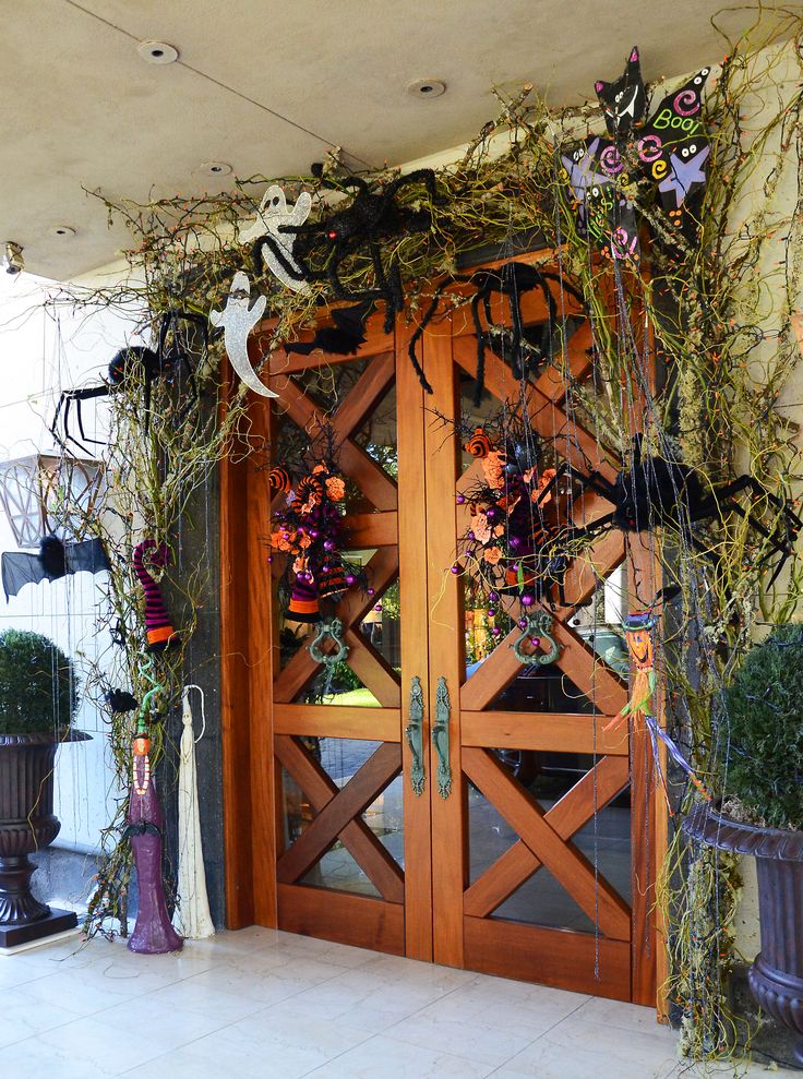 An outstanding and bold Halloween front door done with green twigs, oversized black spiders, ghosts, cats and striped stockings is a playful solution