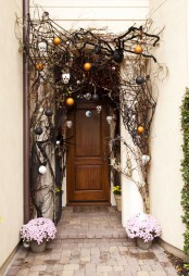 a scary Halloween front door with black branches, black spiders, black and orange ornaments and skulls is a cool idea