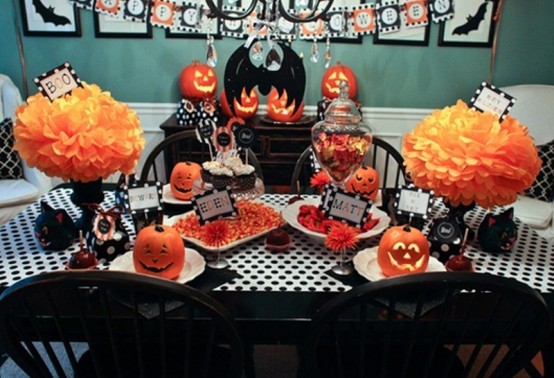 a bold black, white and orange Halloween tablescape with paper pumpkins, black linens and goblets, jack-o-lanterns and lots of sweets