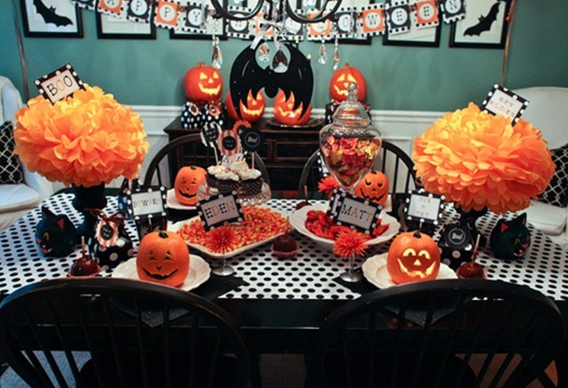 A bold black, white and orange Halloween tablescape with paper pumpkins, black linens and goblets, jack o lanterns and lots of sweets