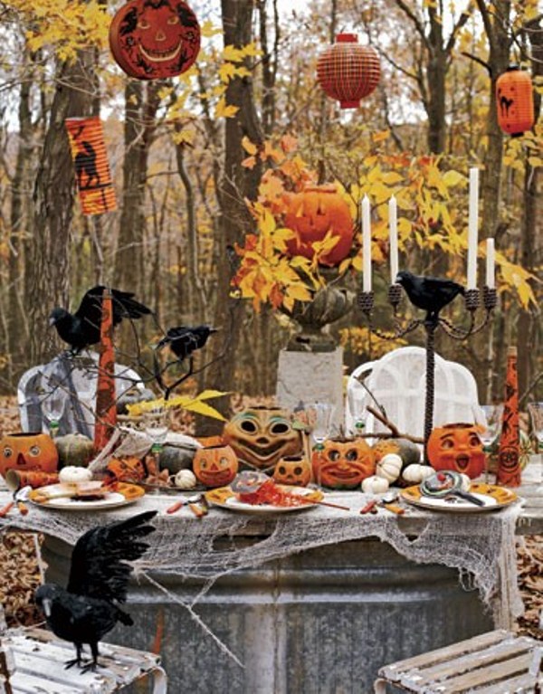 An outdoor Halloween tablescape with jack o lanterns, fall leaves, candles, elegant porcealin, crows and cheesecloth