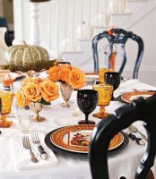 an elegant Halloween tablescape with orange and black plates and glasses, orange roses in gold vases and a metallic pumpkin on a stand