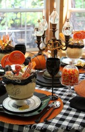 a bright Halloween tablescape in black, orange, white, with a candelabra, black goblets, orange pumpkins and plaid textiles