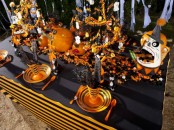 an extra bright blakc, graphite grey and orange Halloween tablescape with orange plates, cutlery, scary pumpkins and faces, lots of candies and witches’ hats