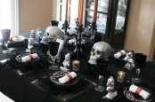 a black and silver Halloween table with black linens, plates and goblets, skulls, candles, a black candelabra with orange candles