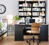 an eclectic bedroom and home office in one with a grey desk, large bookcases for storage, a metal bed and printed bedding