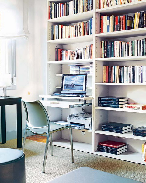 A neutral home office with an oversized bookcase and a built in desk, a black table and a blue pouf and a blue chair