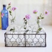 a metal wire basket with vintage bottles and bright blooms is a chic and cool decoration that is vintage and delicate and will bring romance to the space
