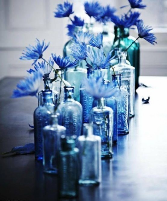 an arrangement of blue bottles with blue flowers is a cool idea for spring or summer decor, they will add color and interest and can be used as a cool centerpiece