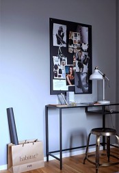 an elegant working space with a black desk that is Vittsjo table, a metal stool, a black memo board with photos and a white table lamp