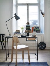 a Nordic working space with a windowsill for storing books, a clock, a black Vittsjo table as a desk, a table lamp and a stained chair
