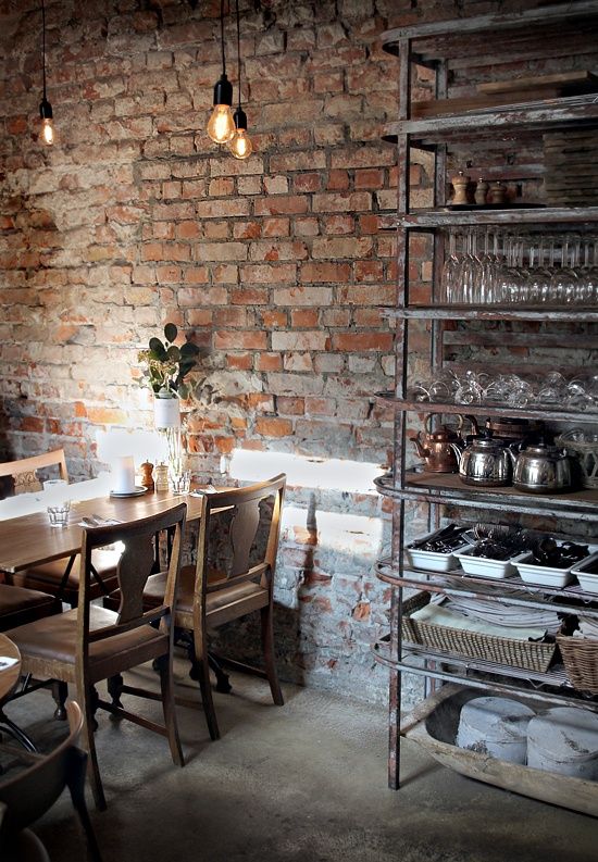a vintage industrial dining room with brick walls, a metal storage unit, a stained table and chairs, hanging bulbs