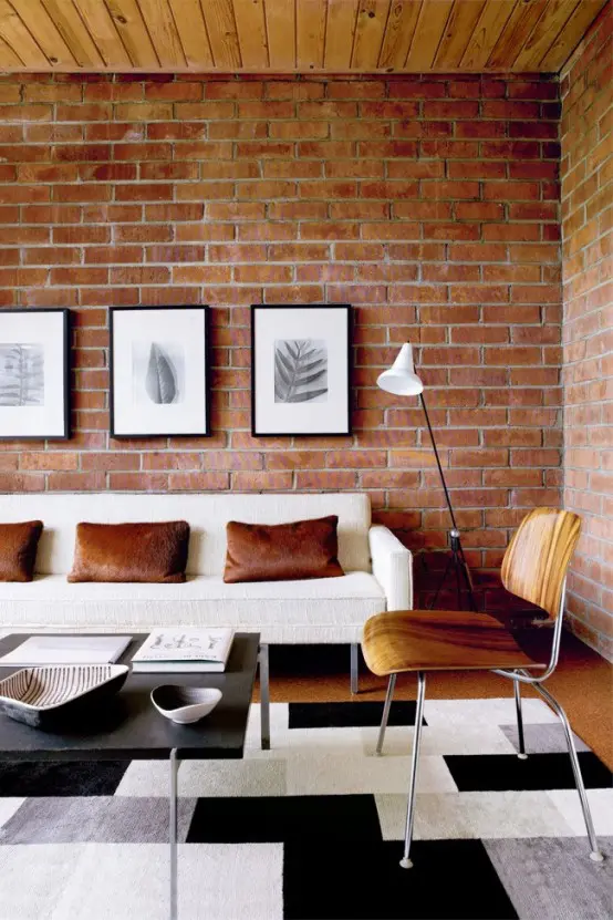 a welcoming modern living room with a red brick statement wall, faux fur pillows and a wooden ceiling