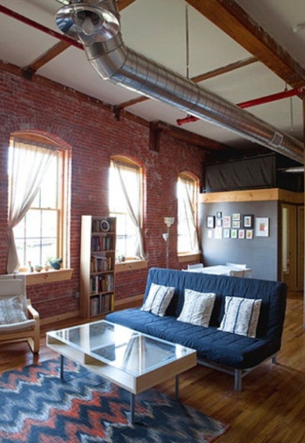 An industrial living room done with red brick walls and metal pipes on the ceiling plus mid century modern furniture