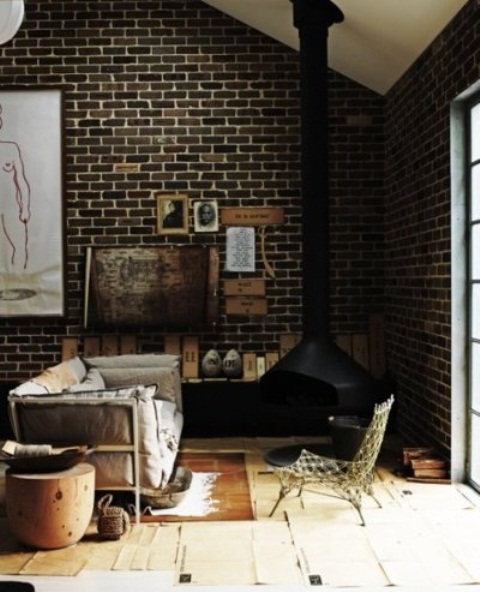 a moody living room with dark brick walls with white grout and a black suspended fireplace plus rugs and wood