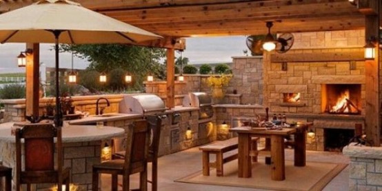 a cozy rustic outdoor bbq area of stone and wood, a sink, a grill, a fireplace and a dining zone next to it