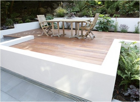a contemporary deck with wooden floors and simple rustic furniture for dining, some planted greenery around