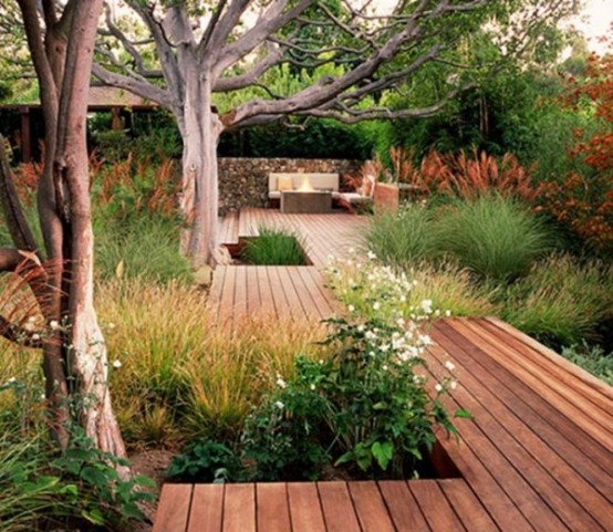 a contemporary deck with grasses growing and a cozy sittign room in the corner, a fireplace and some trees