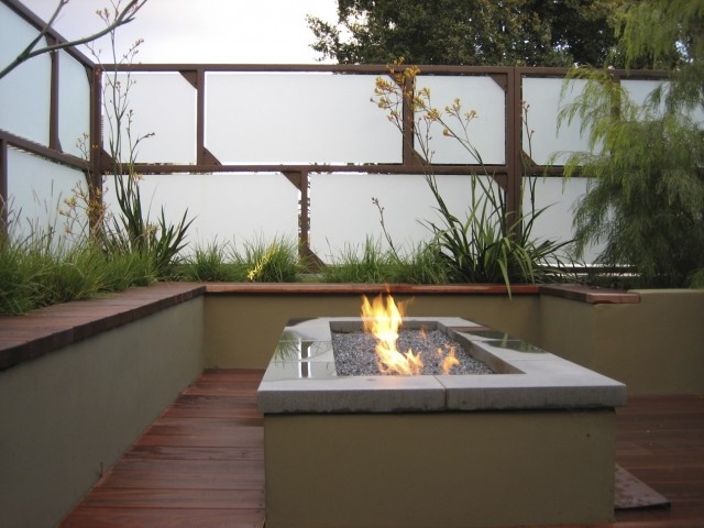 A contemporary deck with a white and wood walls for some privacy, a built in bench, a fire pit and some grasses growing around