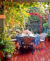 a colorful shabby chic deck with a forged garden furniture set, growing tress and greenery and colorful textiles