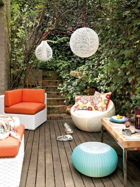 a welcoming and bright deck with a weathered wood floor, colorful furniture, yarn lamps and a cocktail table