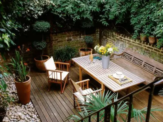 a cozy rustic deck with simple wooden furniture, pebbles and potted greenery plus greenery all around for privacy