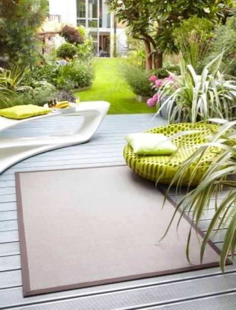 a contemporary deck with a sculptural console, a bright neon chair, a rug and growing greenery and blooms